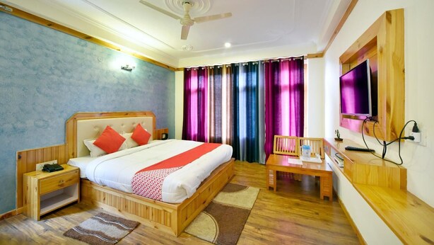 Una habitación de hotel con una cama de madera, un escritorio con silla, un televisor y un ventilador de techo.