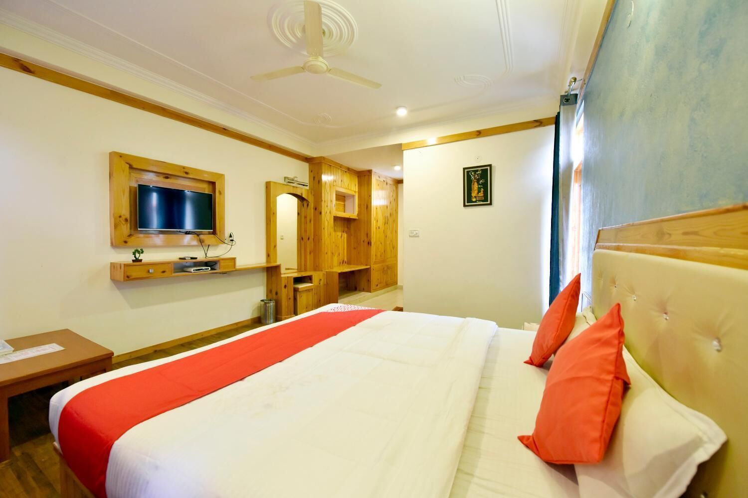 A hotel room with a large bed, wooden headboard, a television mounted on the wall, and a ceiling fan.