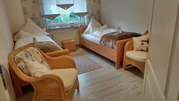 Un dormitorio acogedor con dos camas individuales, una silla de mimbre, una mesita de noche y una ventana con vistas a la vegetación.