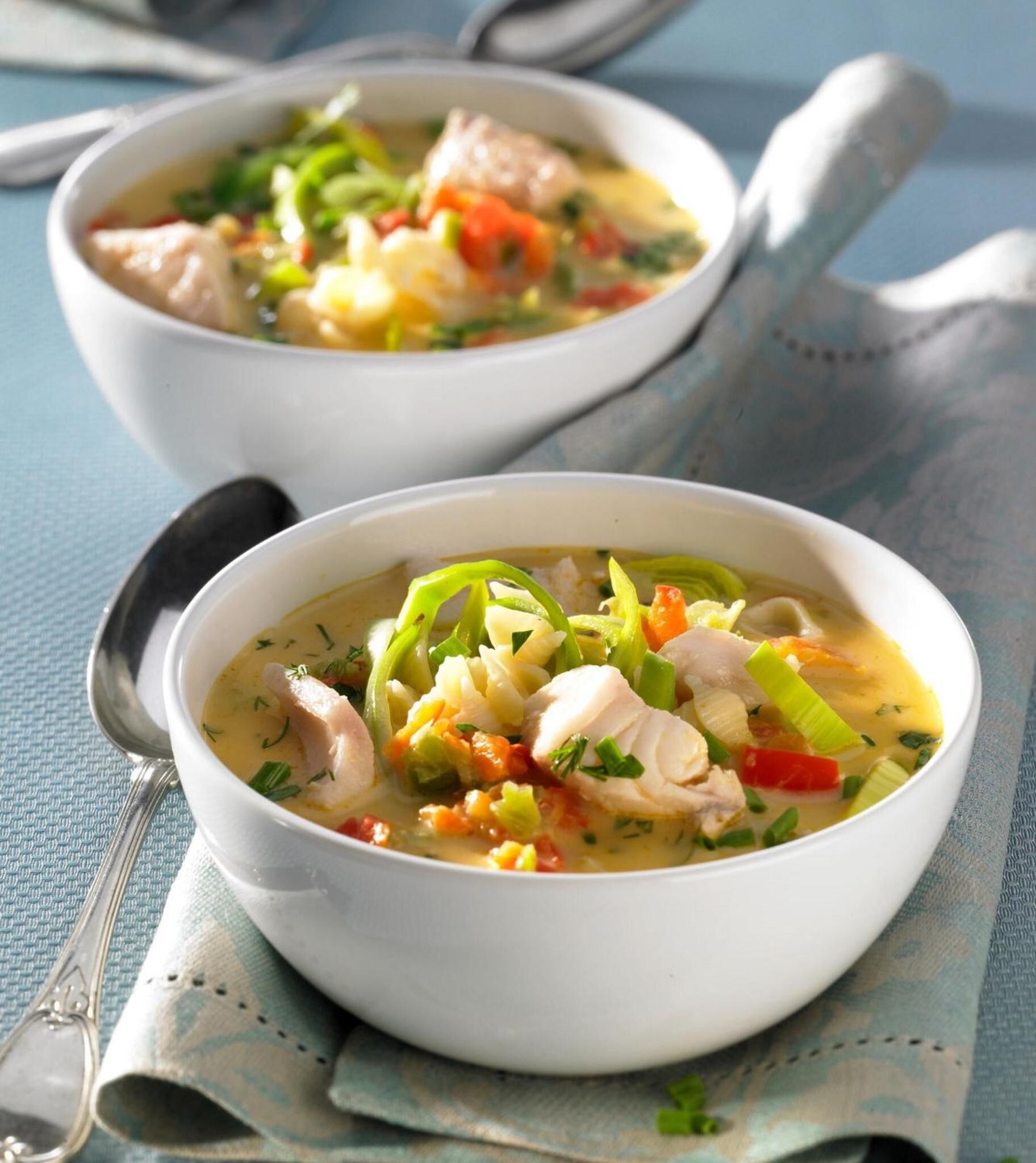 Two bowls of soup with vegetables and chicken on a blue textured surface.