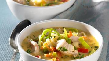 Two bowls of soup with vegetables and chicken on a blue textured surface.