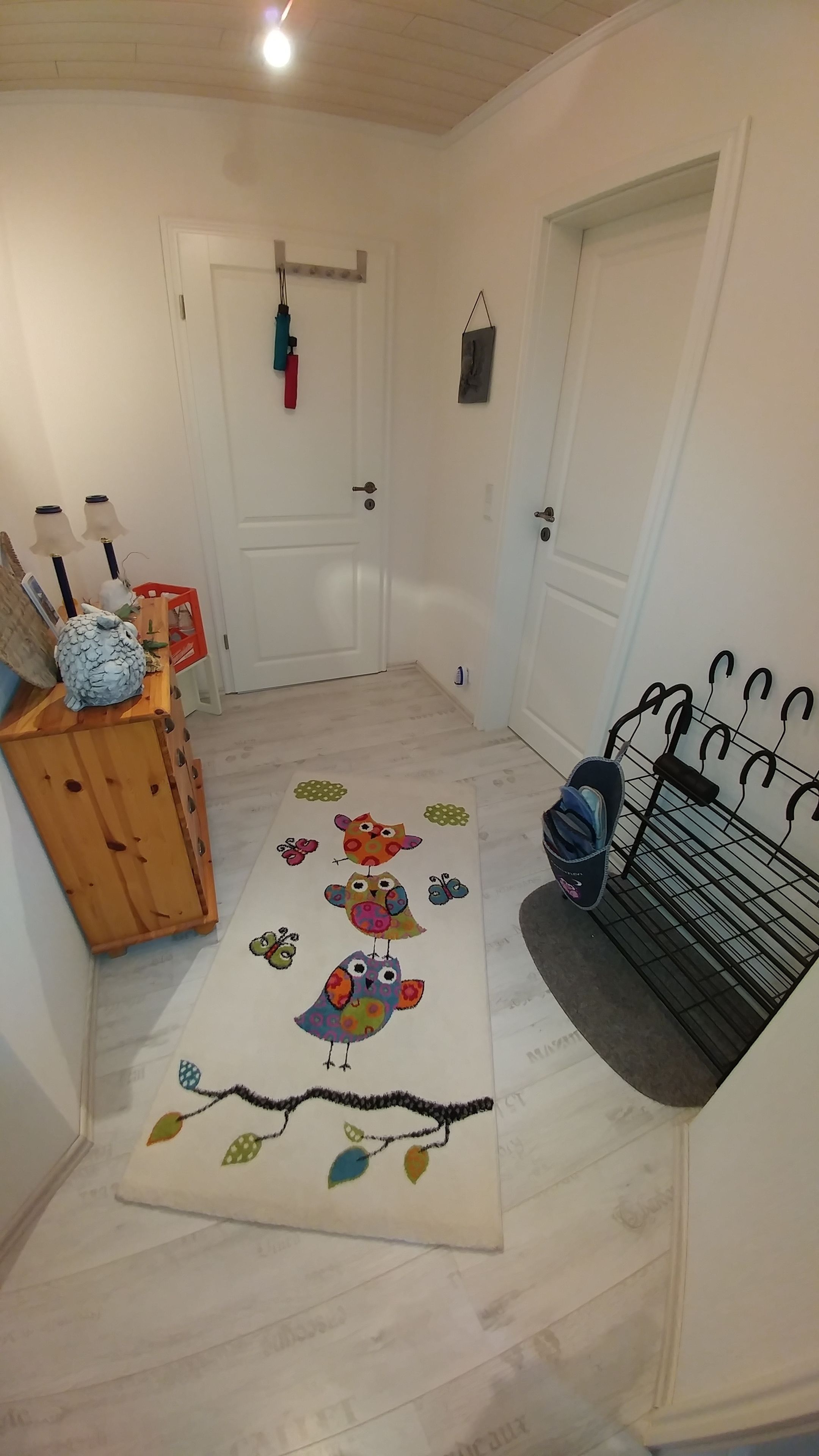 A hallway with a wooden bench, a colorful rug with bird and butterfly designs, and a coat rack.