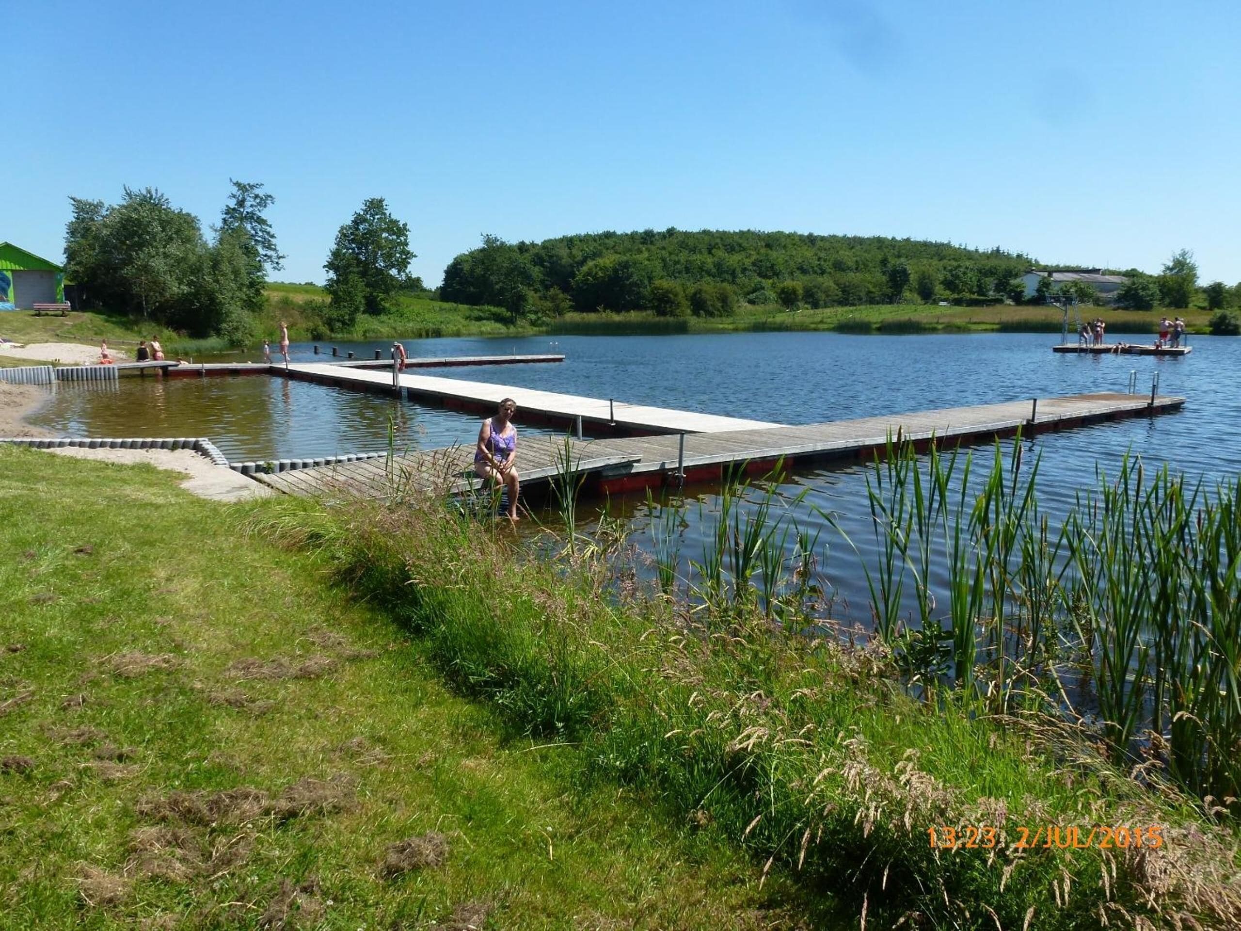 Muelles sobre el lago con gente practicando actividades acuáticas, rodeado de vegetación exuberante y un cielo despejado.