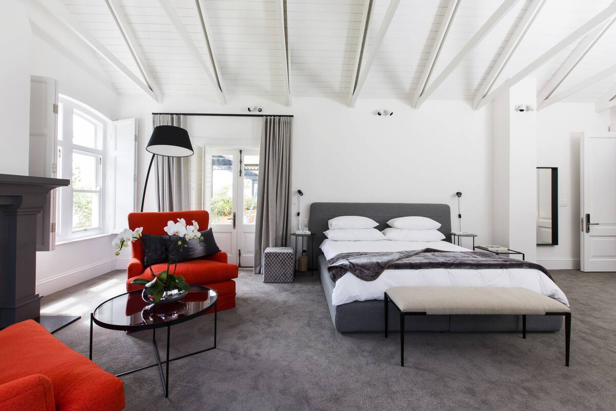 A modern bedroom with a bed, a red armchair, a glass coffee table, and a large window.