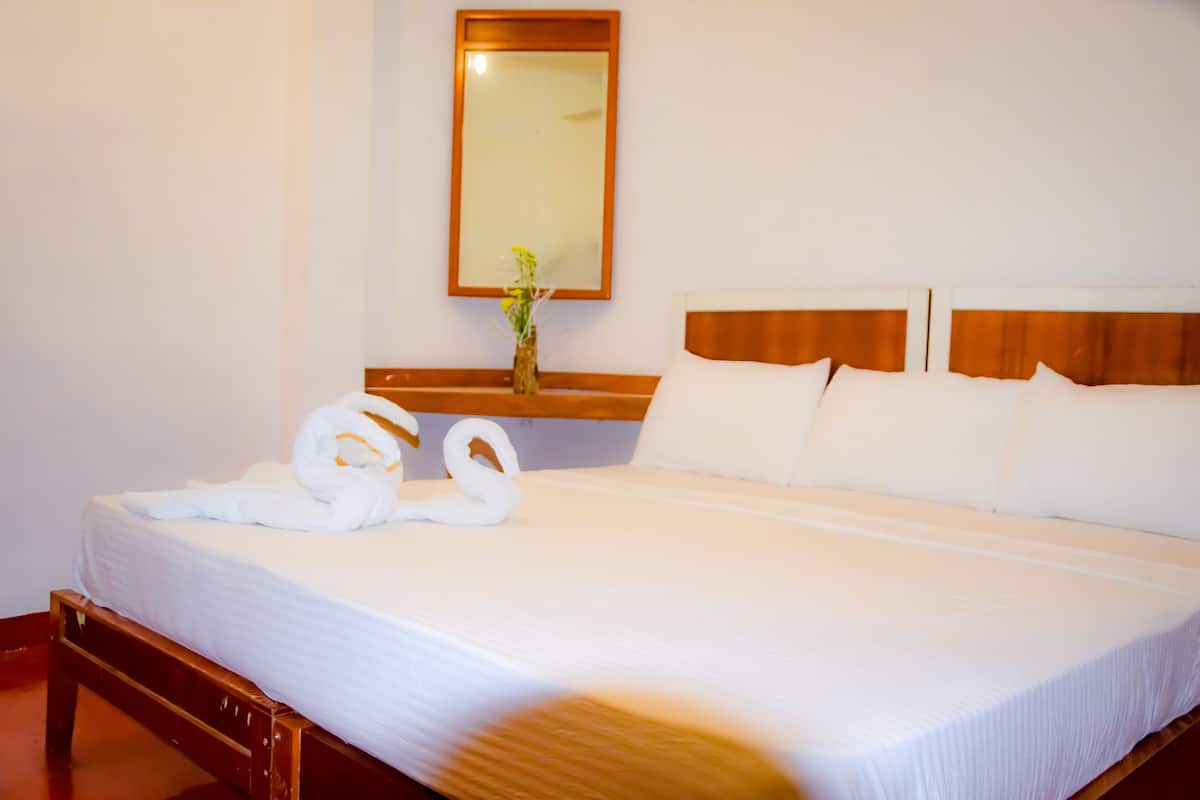 A neatly made bed with white linens, a wooden headboard, and a mirror above it.
