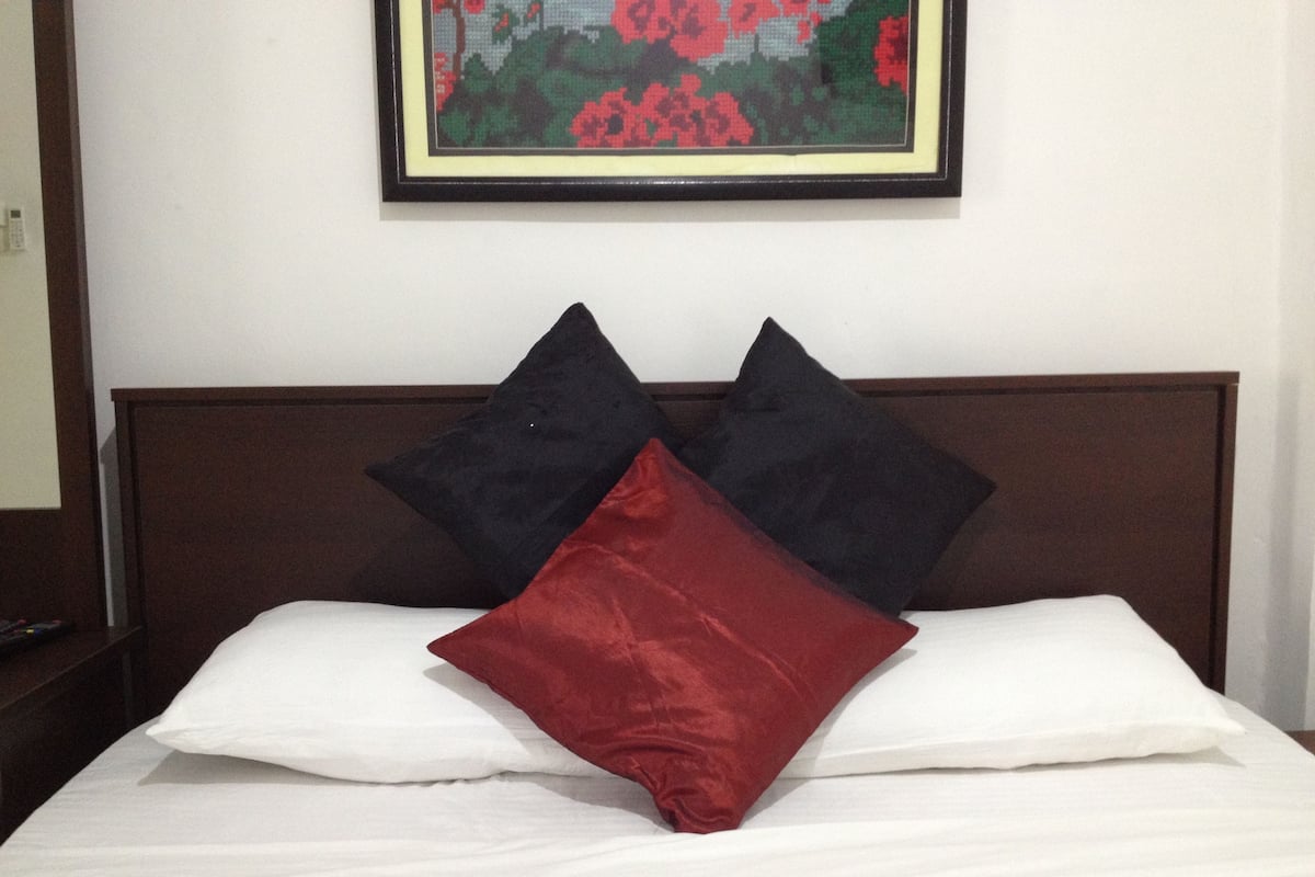 A bed with white sheets and three pillows in black and red.