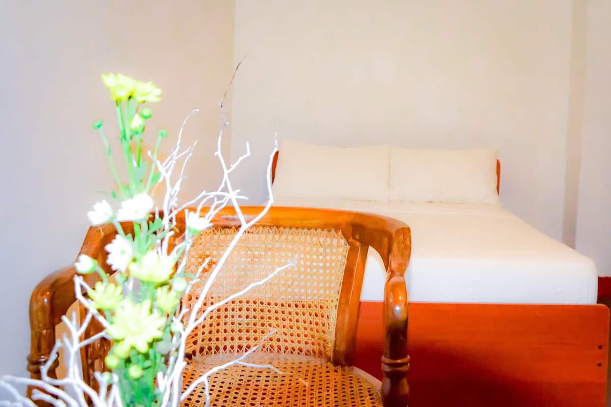 A wooden chair with a woven backrest and a white mattress in a room with plain walls.