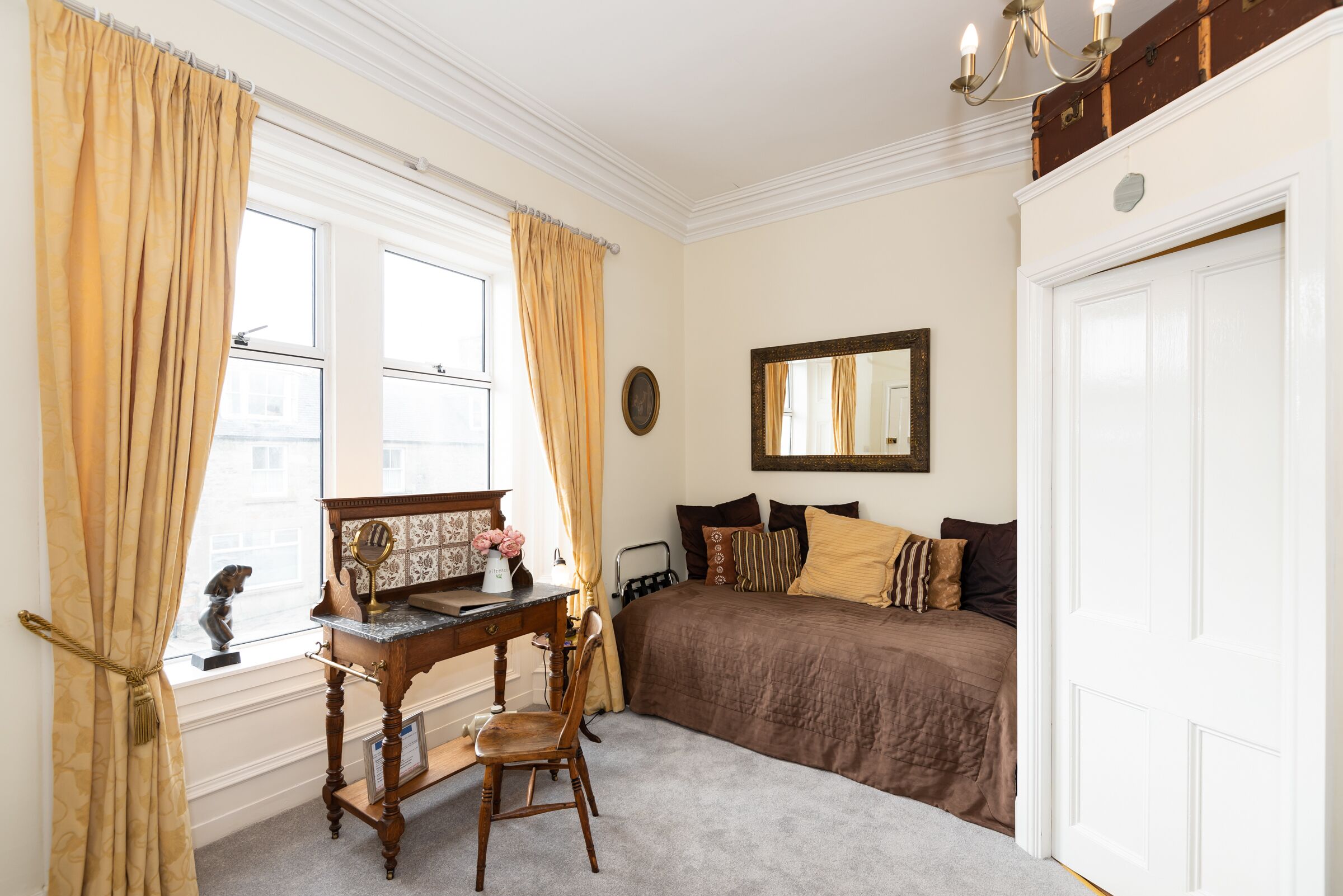 A bedroom with a bed, a desk with a chair, a mirror, and a window with curtains.