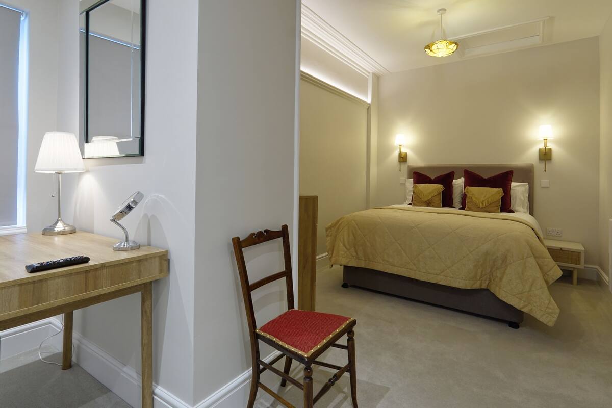 A bedroom with a bed, bedside lamps, a desk with a lamp, a chair, and a mirror.