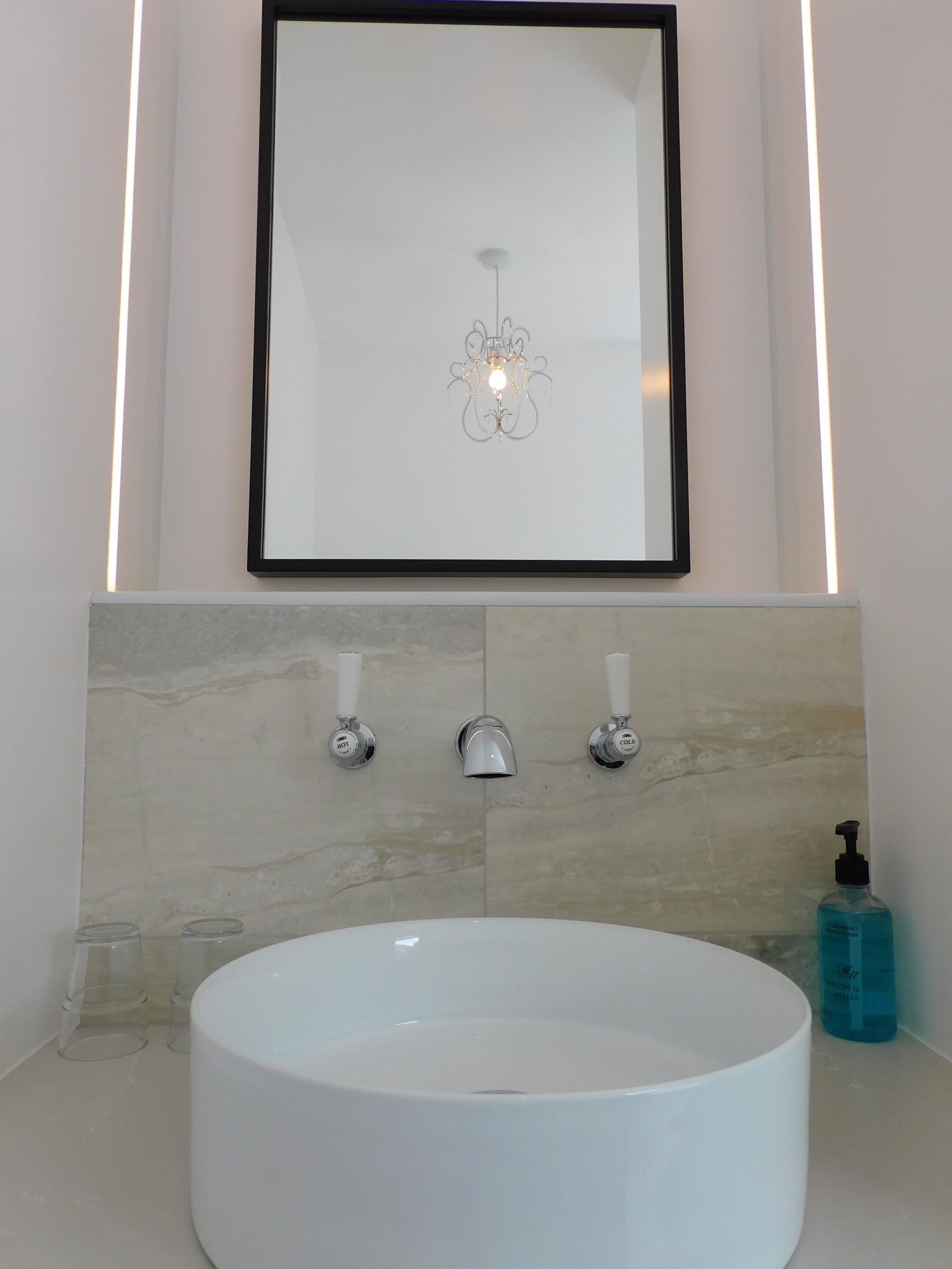 A bathroom with a white sink, a framed artwork above it, and a modern light fixture.