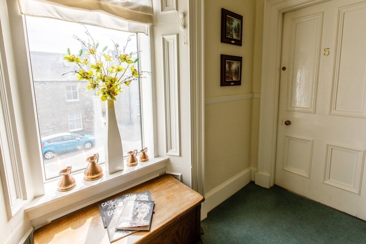 A hallway with a window, a vase with flowers, and a door with the number 5.