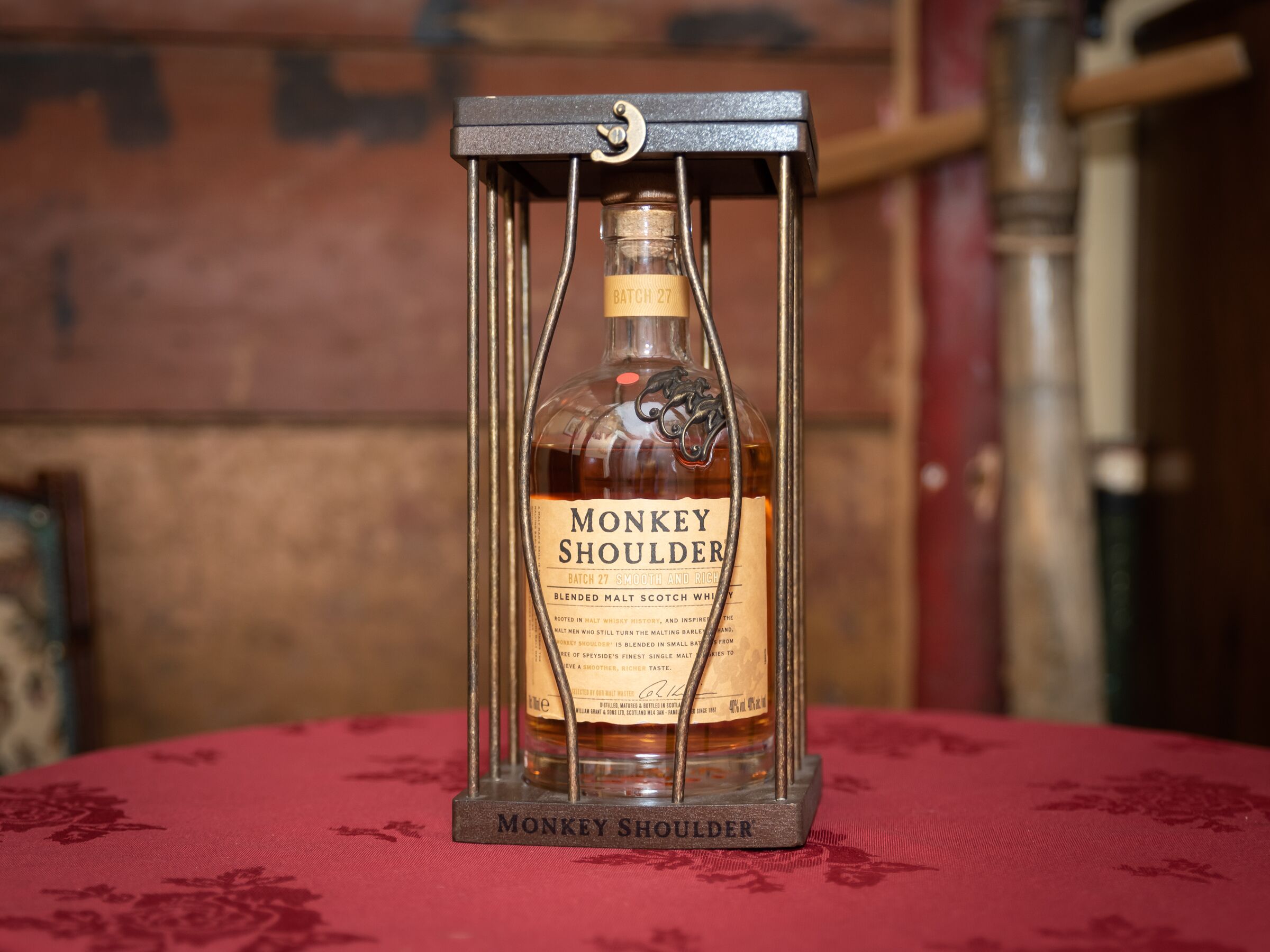 A bottle of Monkey Shoulder whisky in a metal cage on a table.