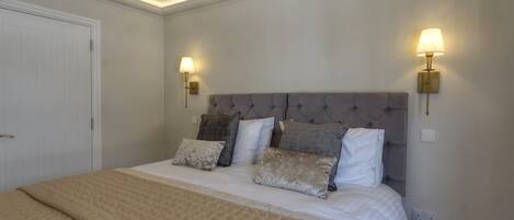 A bedroom with a large bed, two wall-mounted lamps, and a white door.