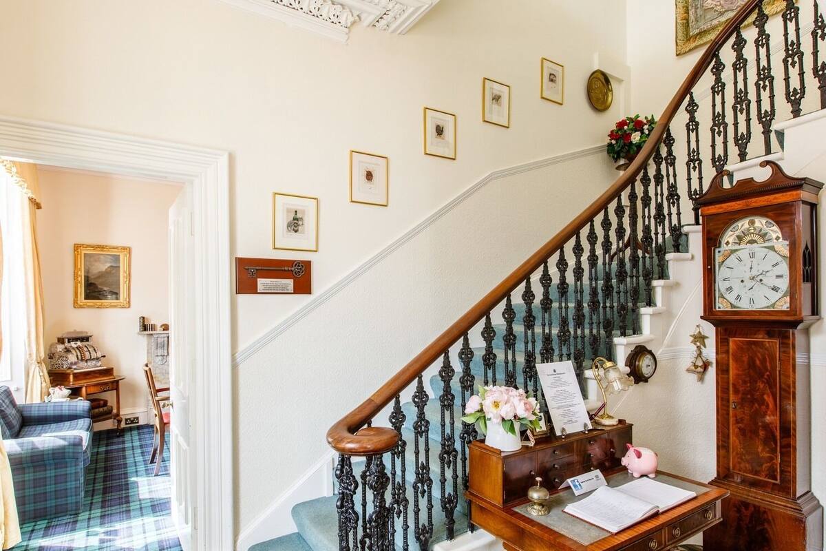 A staircase with ornate black balusters, a wooden desk with a piggy bank, a clock, and framed pictures on the wall.