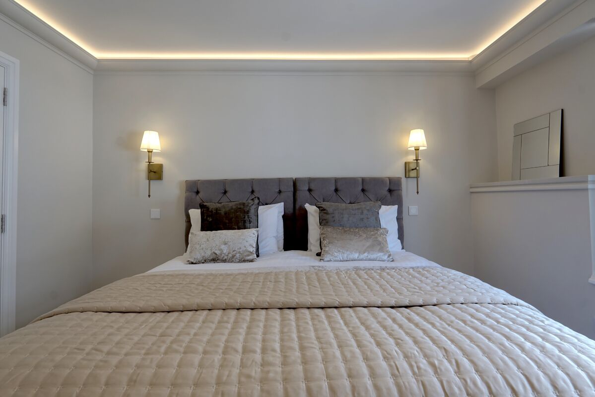 Una cama bien hecha con una colcha acolchada, dos lámparas fijadas a la pared y un cabecero con diseño capitonado.