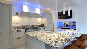 A modern kitchen with white cabinetry, a granite countertop, and a built-in bar area with stools. - The Tannochbrae (Keith)