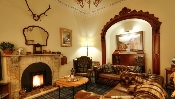 A traditional living room with a fireplace, leather sofas, a plaid carpet, and a decorative mirror. - The Tannochbrae (Keith)