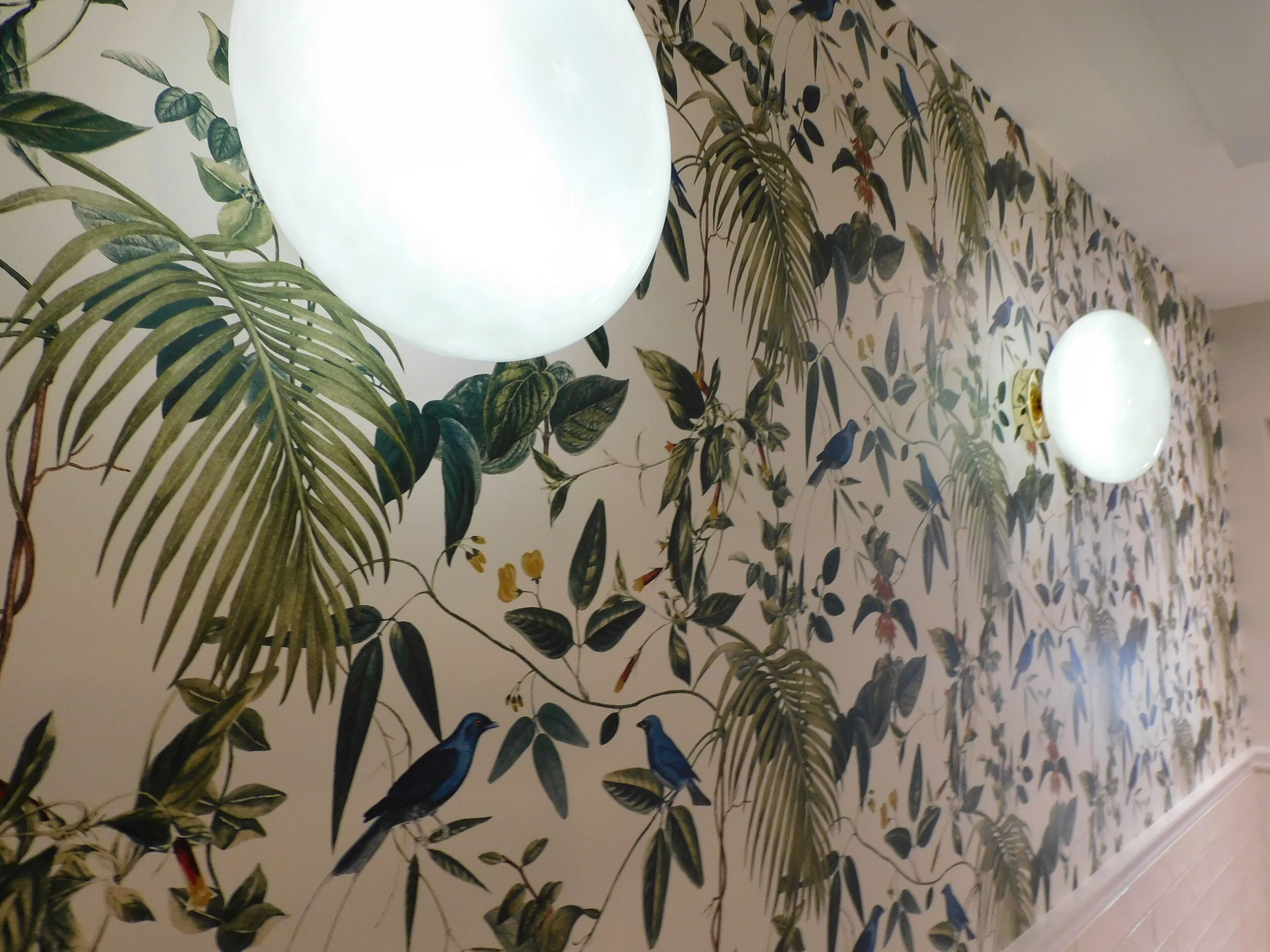 Een muur met een muurschildering van bloemen en vogels, twee hangende bolvormige lampen, en een betegelde vloer.