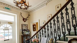 A grand staircase with ornate black balusters, a chandelier, and a clock. - The Tannochbrae (Keith)