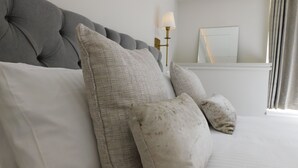 A neatly made bed with a grey upholstered headboard and several pillows. - The Tannochbrae (Keith)