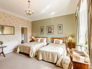 A hotel room with two beds, a chandelier, a mirror, and artwork on the walls. - The Tannochbrae (Keith)