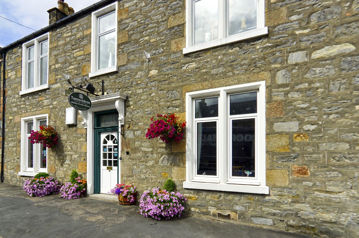 A stone building with a green door, white windows, and flower boxes.