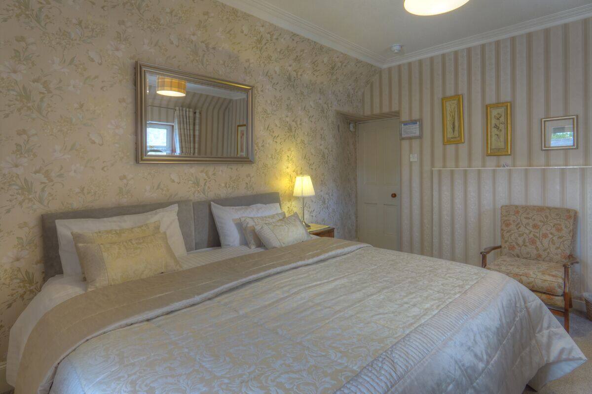 A neatly made bed with a headboard, a bedside lamp, and a chair.