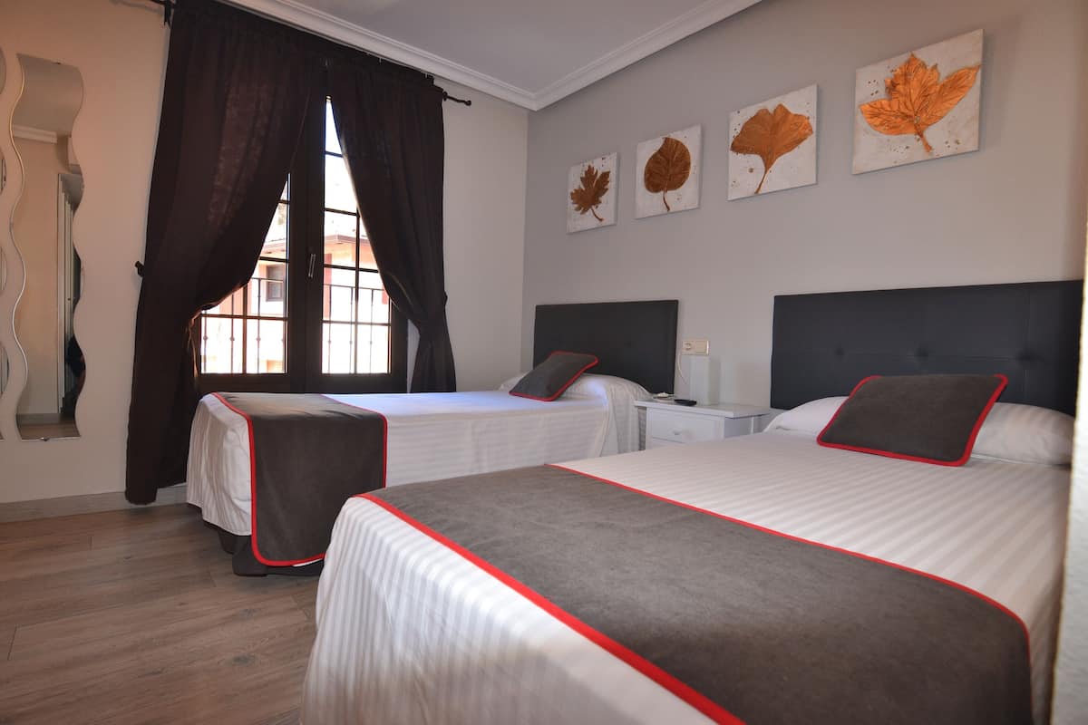 A hotel room with two beds, a window with curtains, and leaf artwork on the wall.