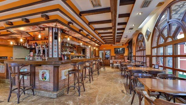 Zona de bar amb tamborets de fusta, un taulell de maó i una varietat de botelles i gots.