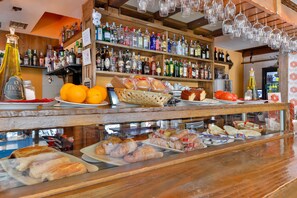 A bar area with shelves of various liquor bottles, a display of bread and pastries, and hanging glasses. - Hostería El Bodegón De Gredos (Arenas de San Pedro)
