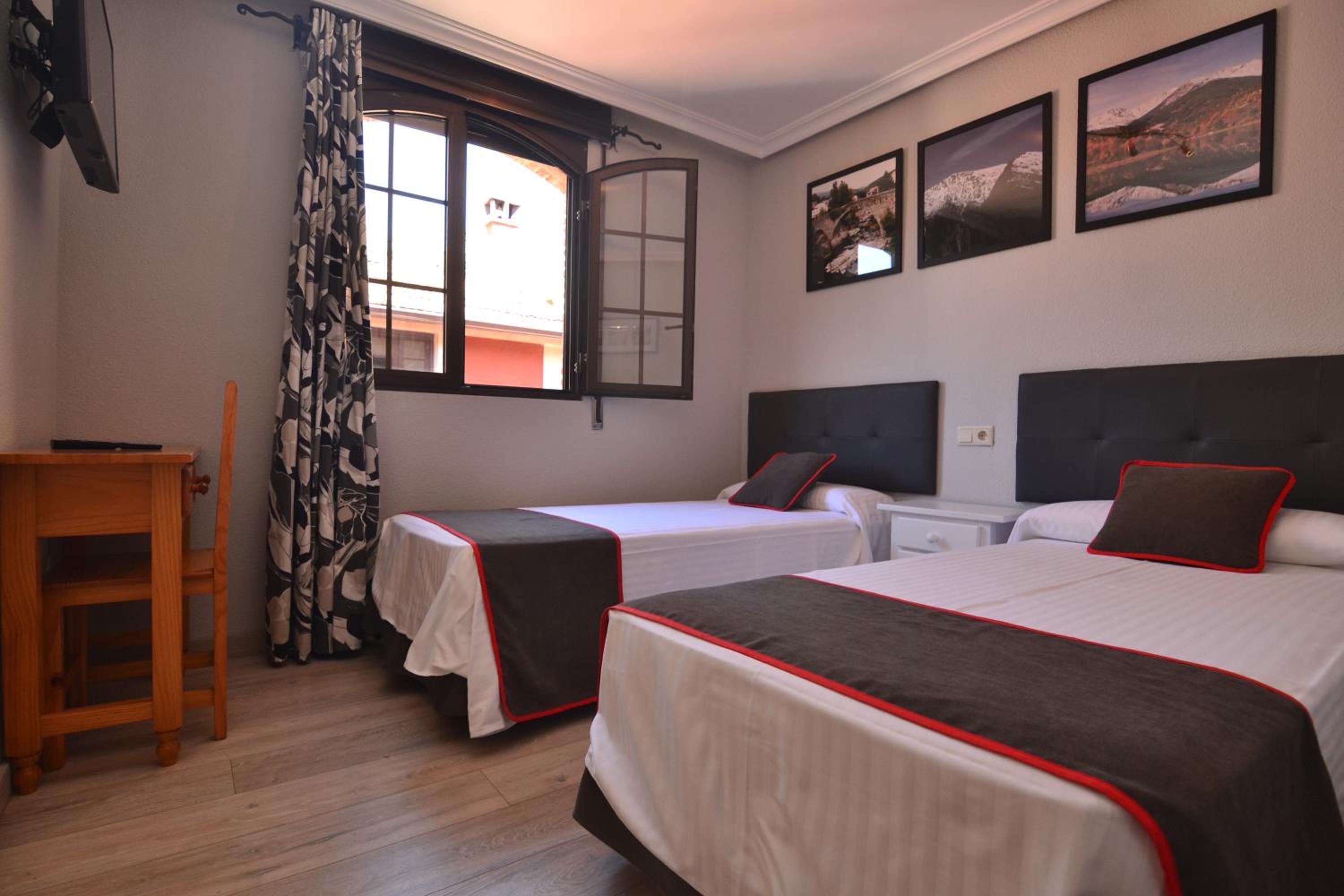 Una habitación de hotel con dos camas, una silla de madera, una mesita y una ventana con cortinas.