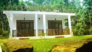 A white building with two large windows and a wooden fence, surrounded by lush greenery.