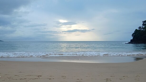 A beach with calm waves, a clear sky, and a distant landmass.