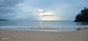 Una playa con olas tranquilas, cielo despejado y una masa de tierra a lo lejos.