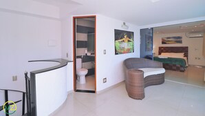 Ein modernes Hotelzimmer mit einer gebogenen Couch, einem separaten Badezimmer und einem Bett mit grüner Decke.