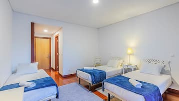 Quarto de hotel com três camas, piso de madeira e porta que dá para outro quarto.