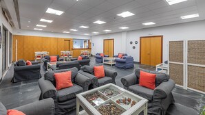 A conference room with grey sofas, red cushions, a glass coffee table, and a wooden panel wall.