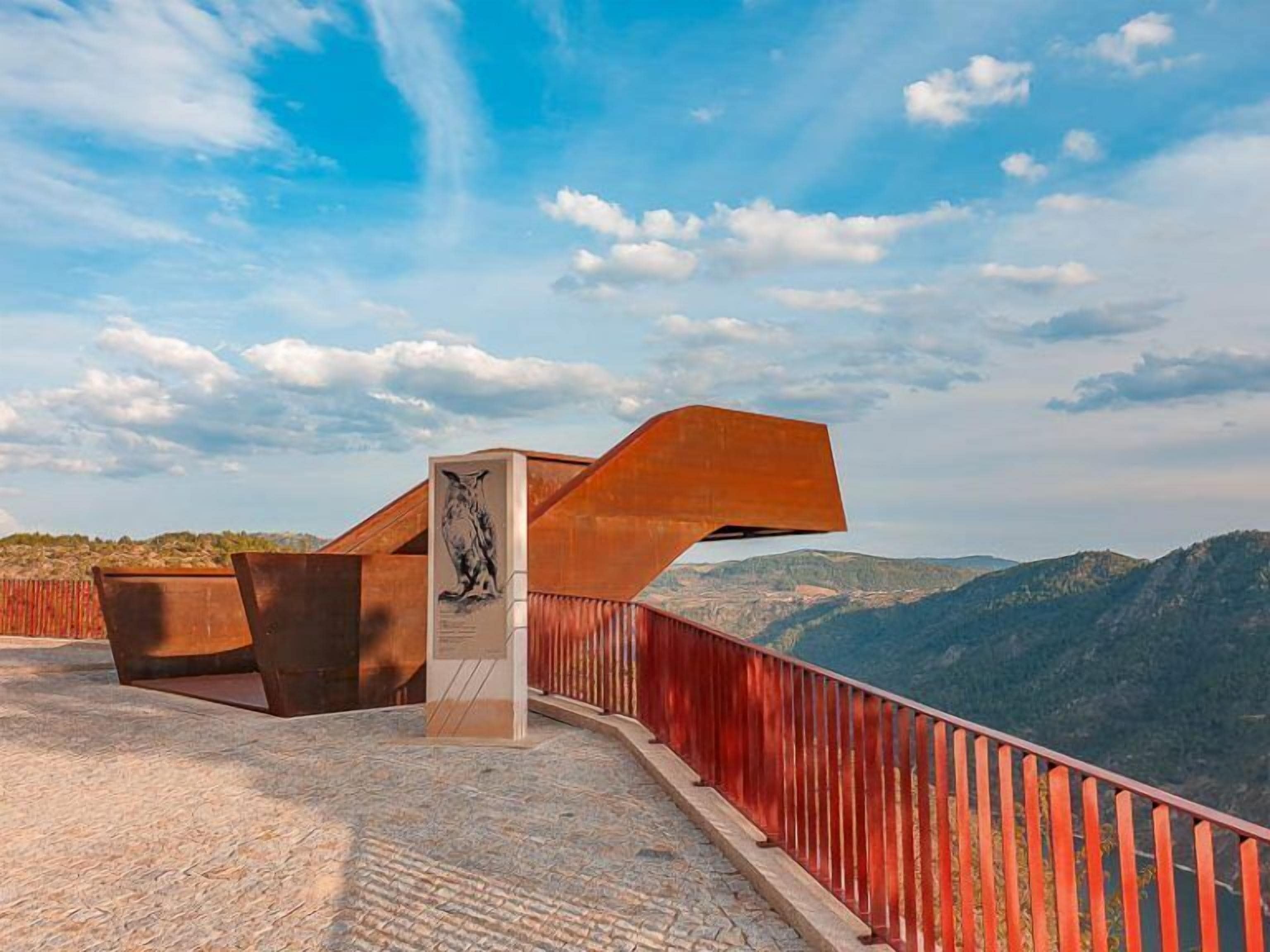 A metal structure with a plaque, a red railing, and a mountainous landscape in the background.