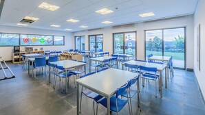 A classroom with tables and chairs, large windows, and educational posters.