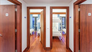 A hotel corridor with wooden doors numbered 113 and 114, leading to rooms with bunk beds and a visible bathroom.