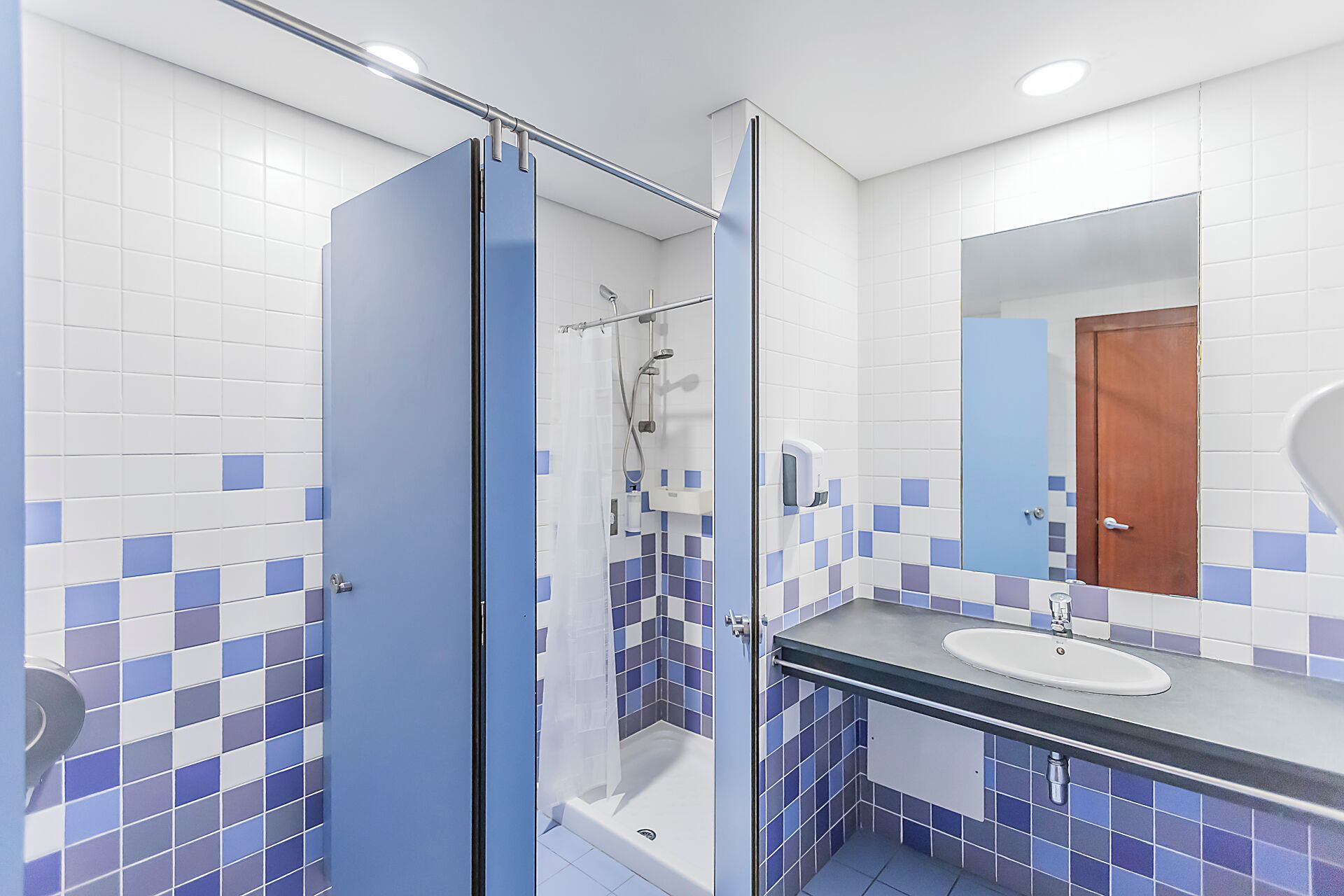A bathroom with a glass-enclosed shower, a sink with a mirror, and tiled walls.