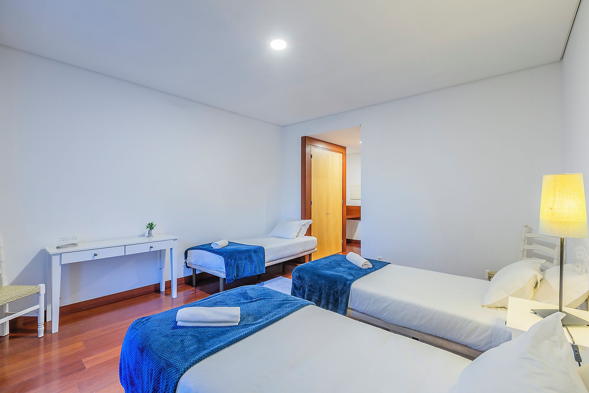 Habitación de hotel con dos camas, un escritorio, una silla, una lámpara y un armario.