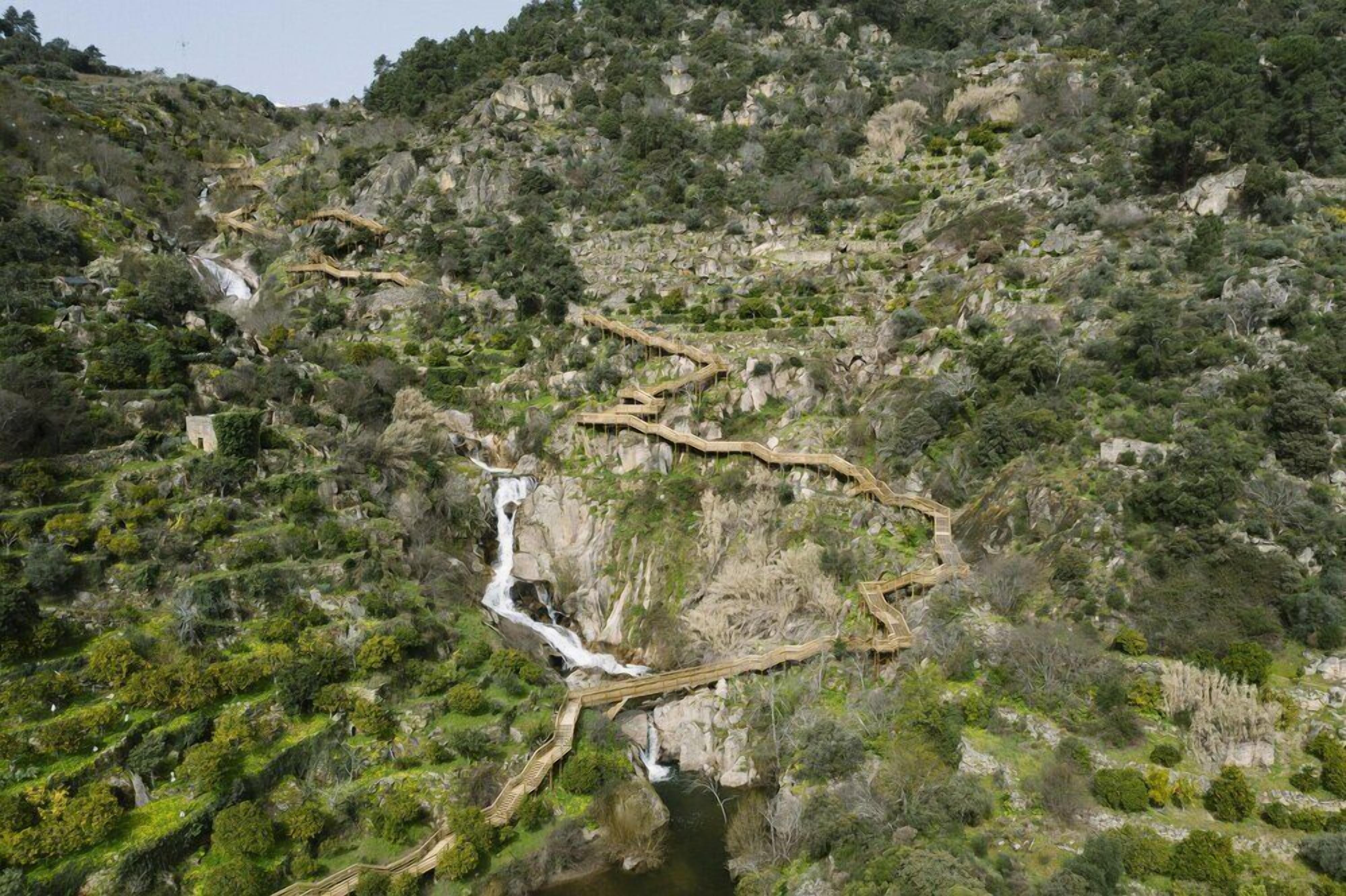 Un paysage montagneux avec un pont en bois sinueux et une cascade.