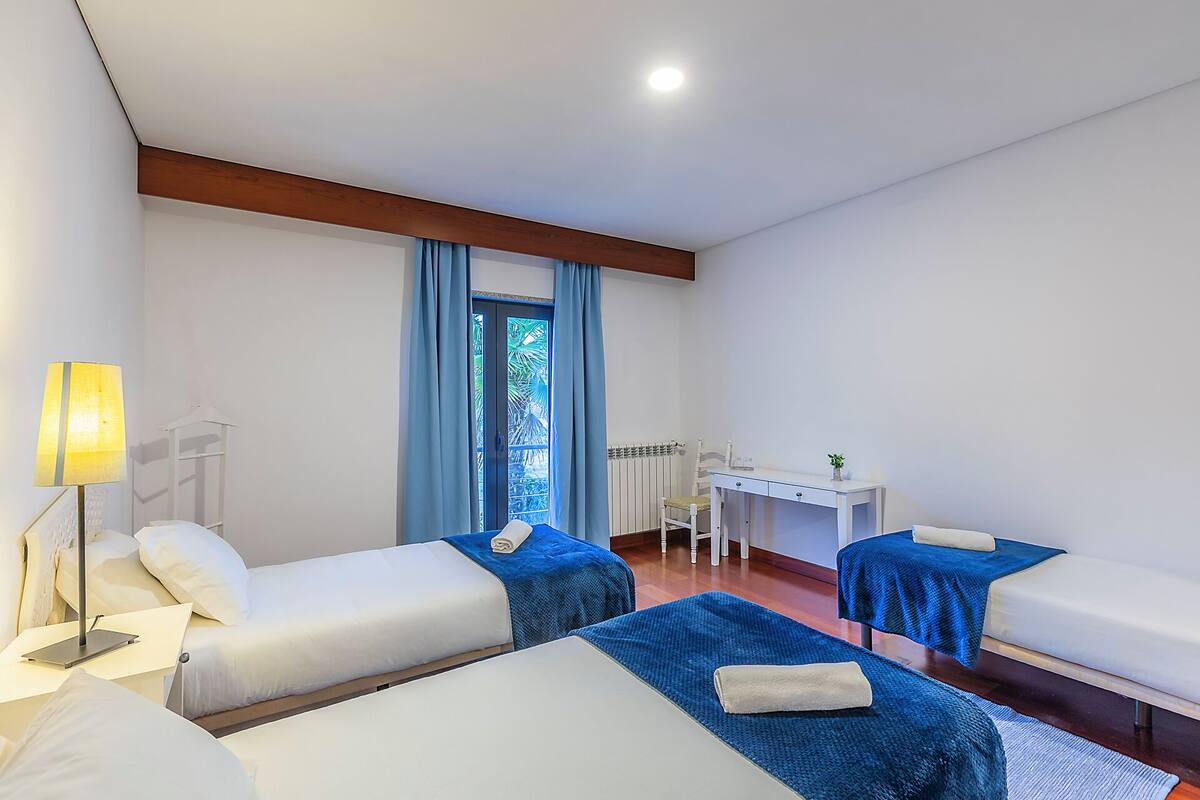 Une chambre d’hôtel avec deux lits, un bureau, une chaise et une fenêtre avec des rideaux.