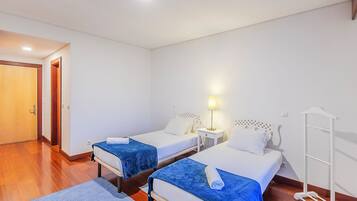A hotel room with two beds, a nightstand with a lamp, a wooden floor, and a white wall.