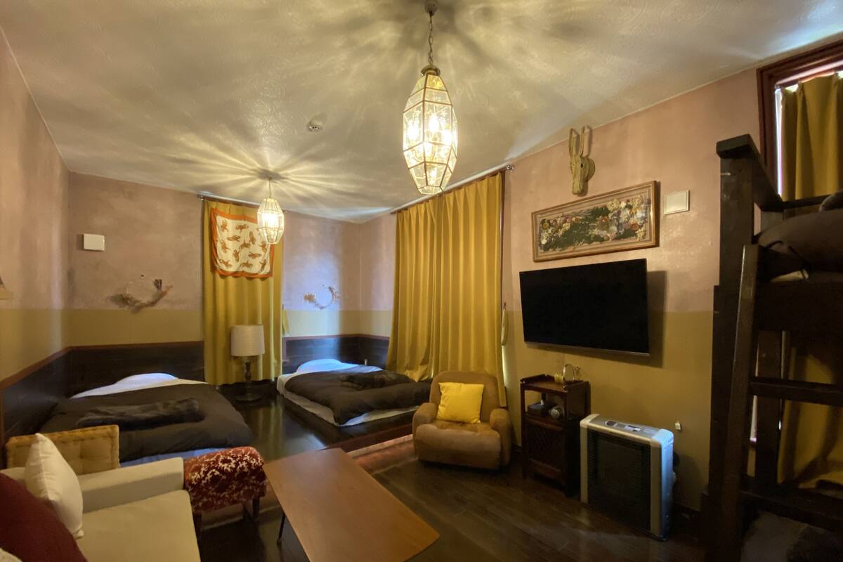 A hotel room with two beds, a sofa, a TV, a heater, and a chandelier.