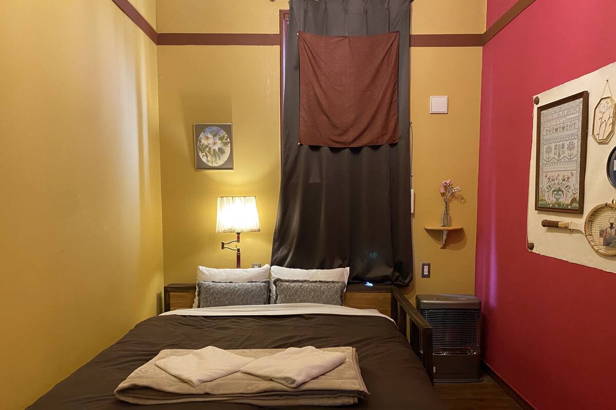 A hotel room with a bed, a nightstand with a lamp, a window with a curtain, and wall decorations.