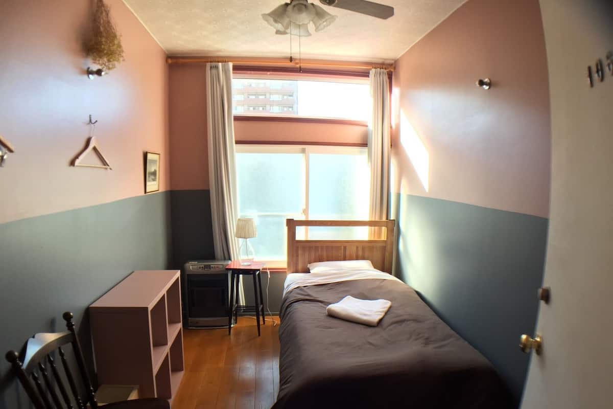 A bedroom with a bed, a desk, a chair, a heater, and a window with curtains.