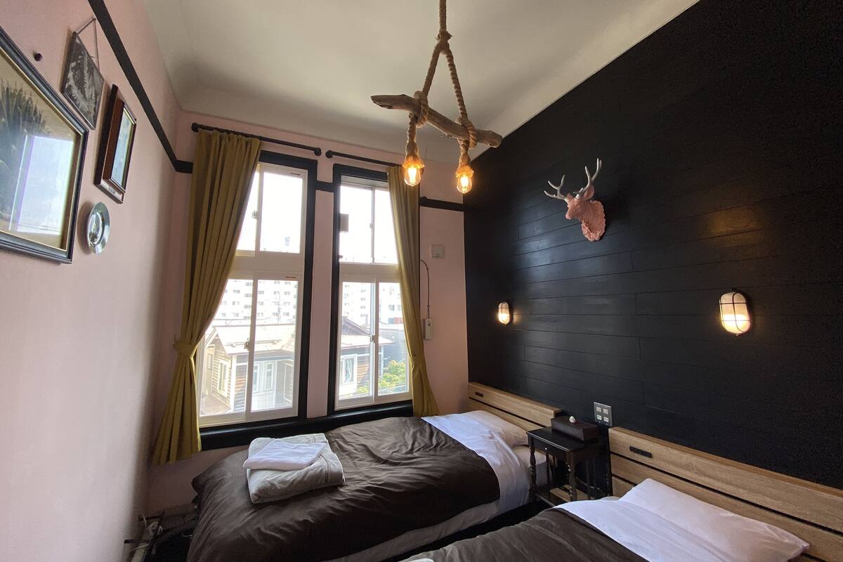 A bedroom with two beds, a ceiling fan, a wall-mounted deer head decoration, and a window with curtains.