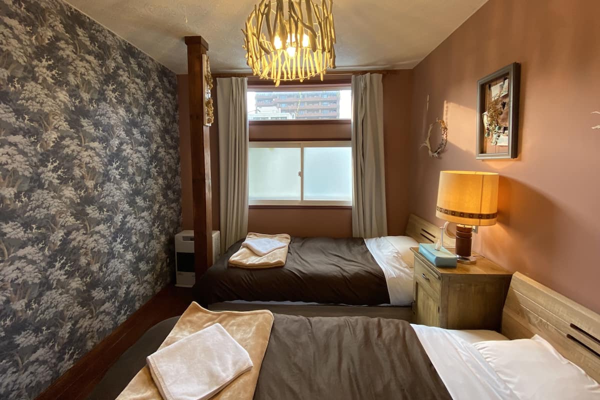 A hotel room with two beds, a chandelier, a window with curtains, a bedside lamp, and a framed picture on the wall.